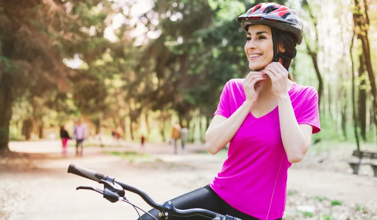 A woman on a bike putting on a helmet.