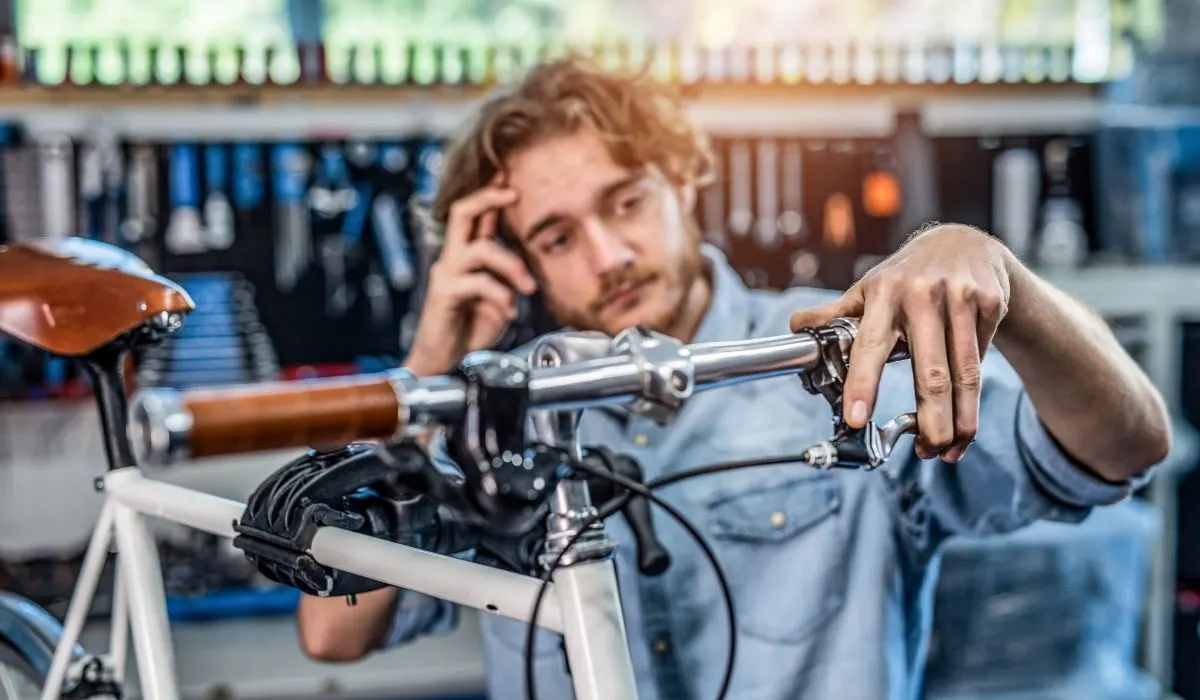 A man with his hand on the hand break of a bike scratching his head with the other hand. 