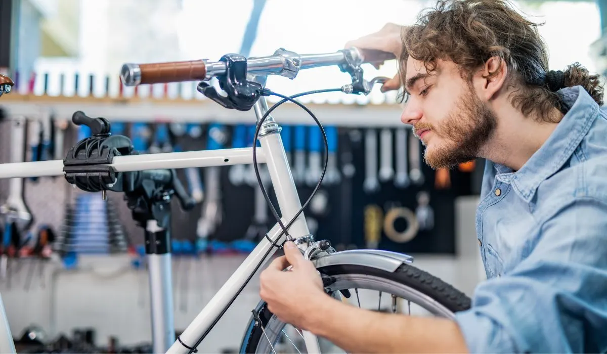 A man inspecting the brakes on a bike, with one hand on the hand brake, and another on the wheel mechanism. 