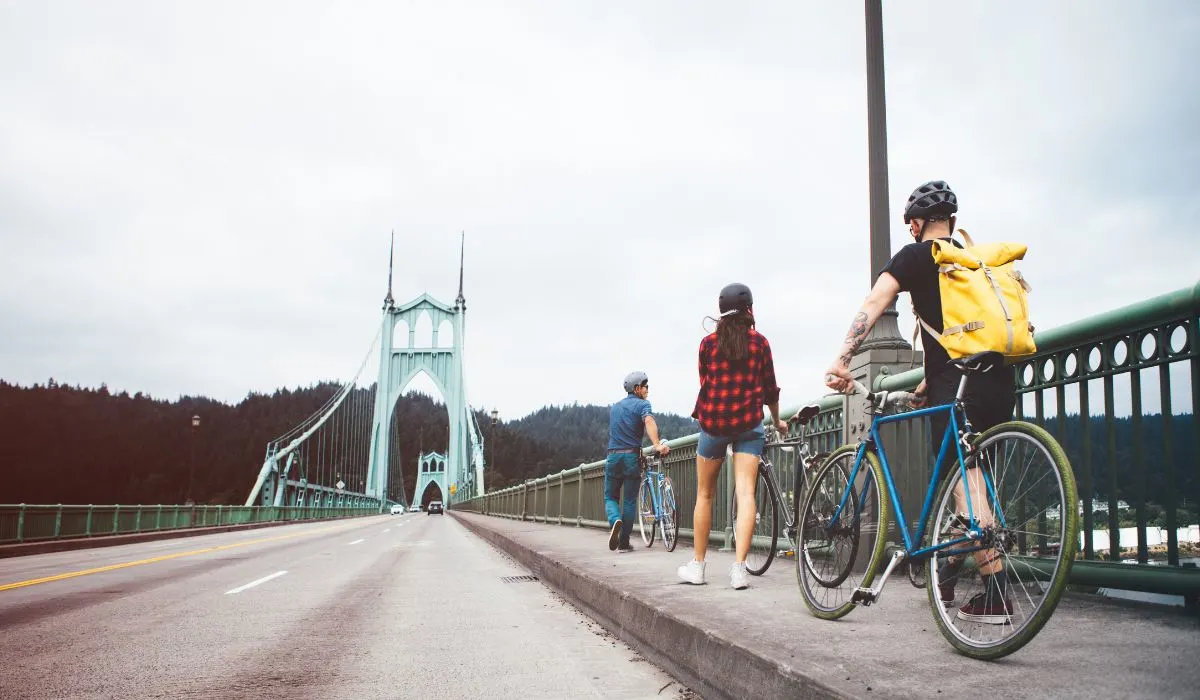 People riding their bikes across a bridge, on man with a yellow weather proof backpack on. 