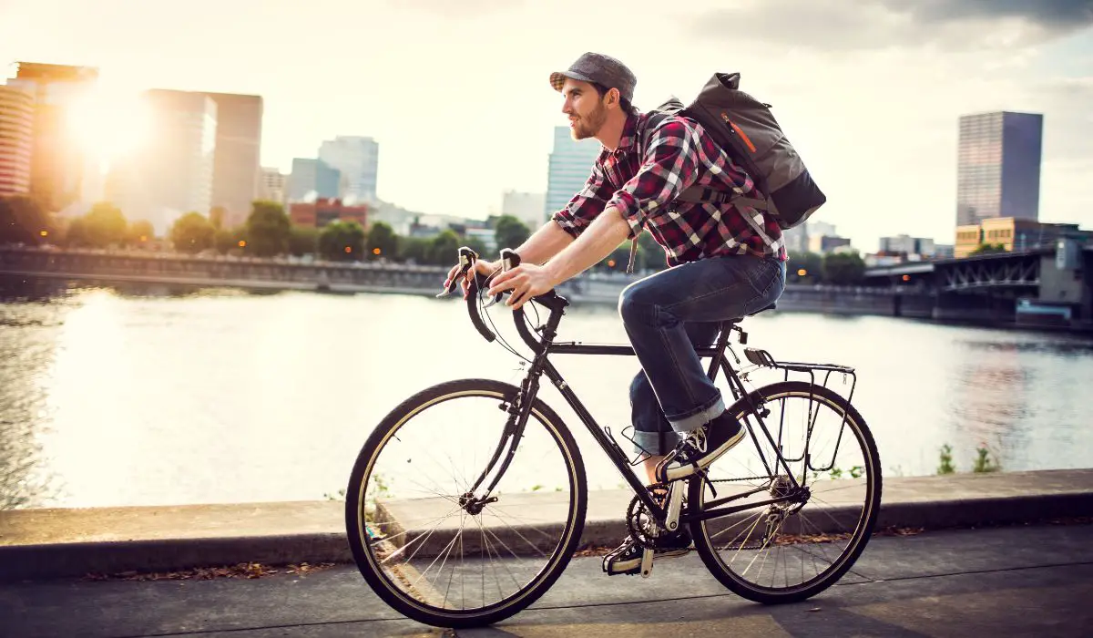 A man riding his bike with a backpack next to a rivier in a city. 