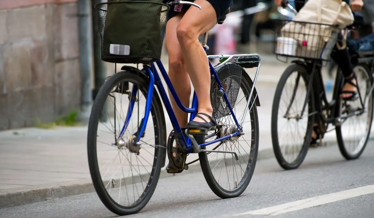 2 bikes riding in the city, each have a front basket and a back rack. 