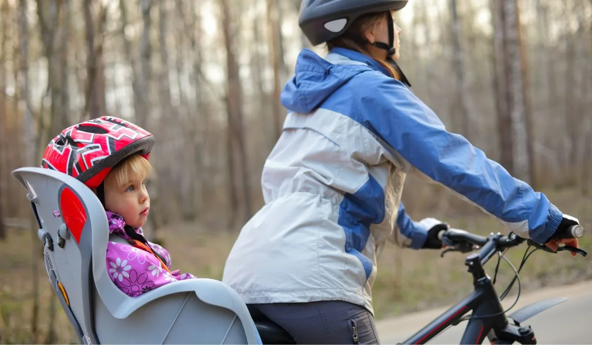 A person riding a bike with a child in a child seat in the back of the bike seat, who is also wearing a helmet. 