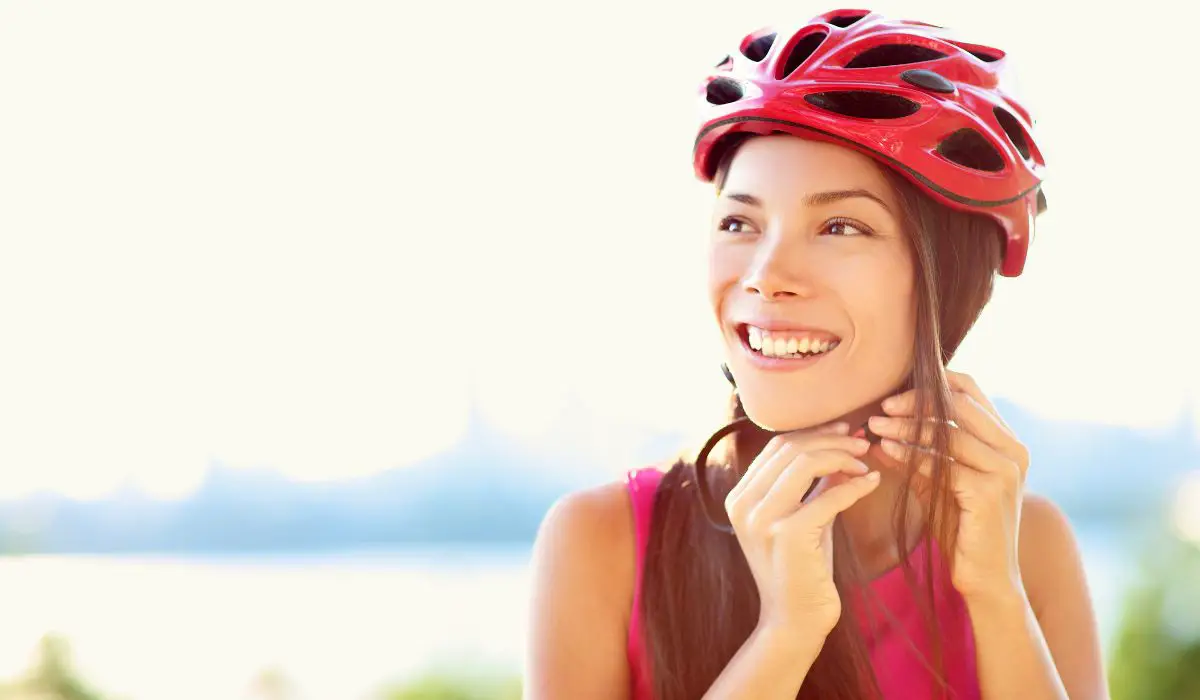 A woman snapping on a red helmet to be ready for a bike ride. 