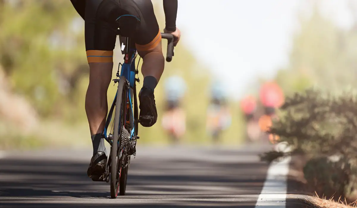 Back view of a man riding a bike on a road, wearing padded shorts. 