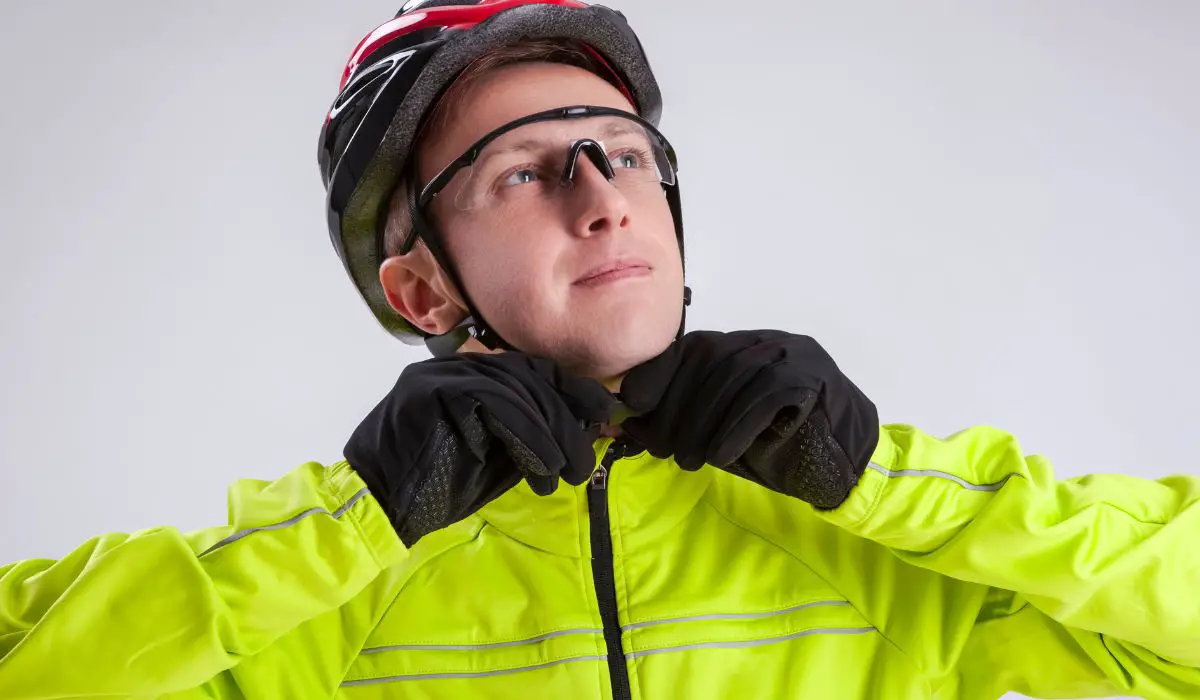 A man strapping on a bike helmet, wearing goggles and a bike coat and gloves. 