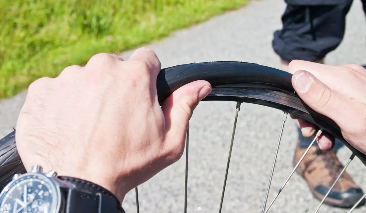 A person trying to get a bike tire off of the wheel without a tool. 