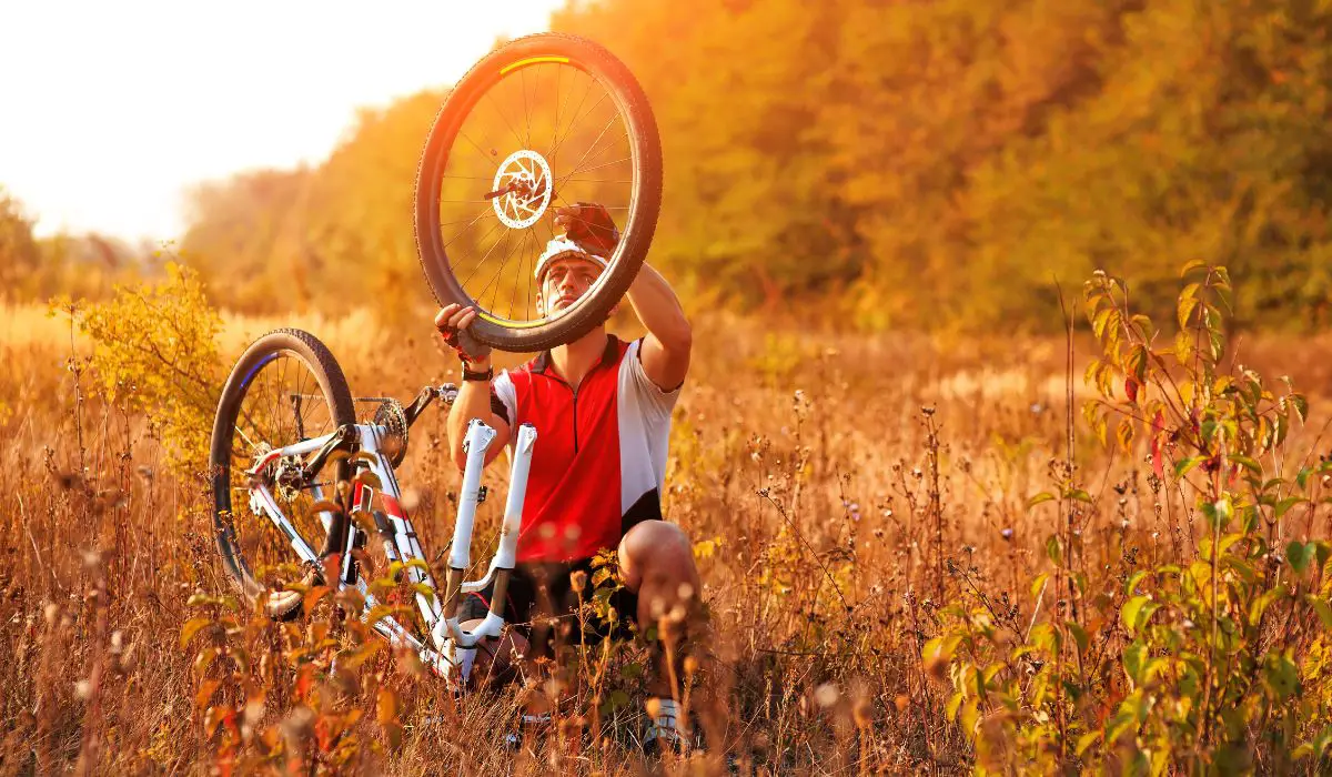 A man in a field with his bike upside down, inspecting the tire is off. 
