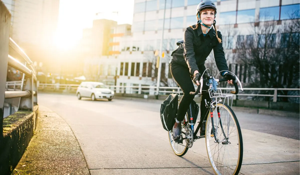 A woman commuting to work on a bike riding in the city with panniers for storage on each side of the back of her bike. 