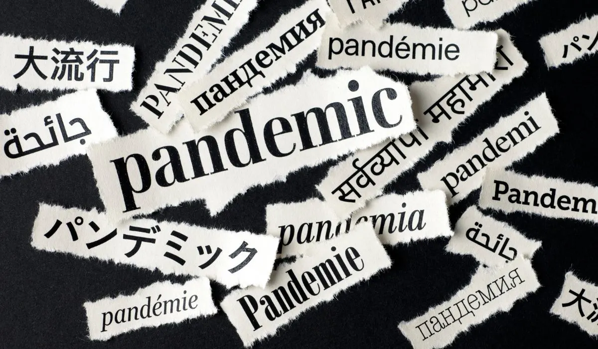 A black background with words written on torn out paper, all saying pandemic in different languages.