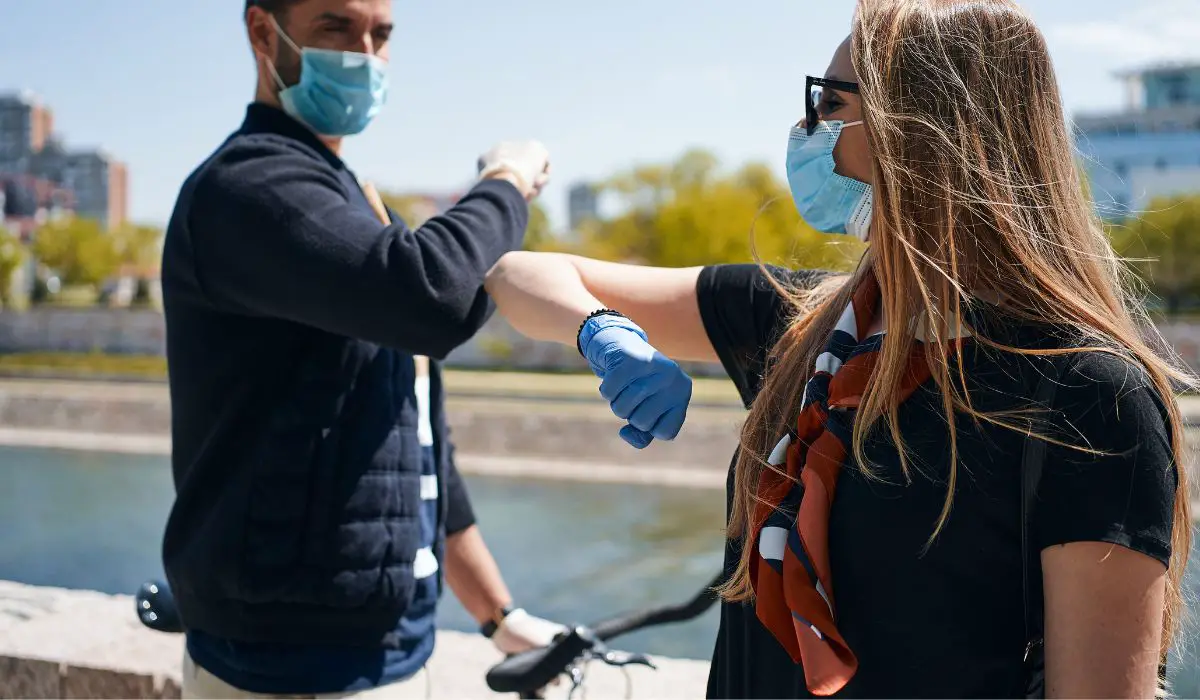 A person stopped on their bike, doing a social distance elbow bump with a friend both wearing masks.