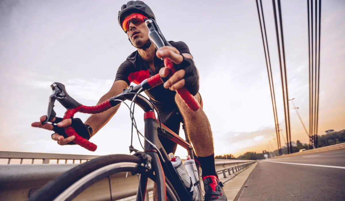 A man cycling across a city bridge with full gear on including a short sleeved cycling jersey.