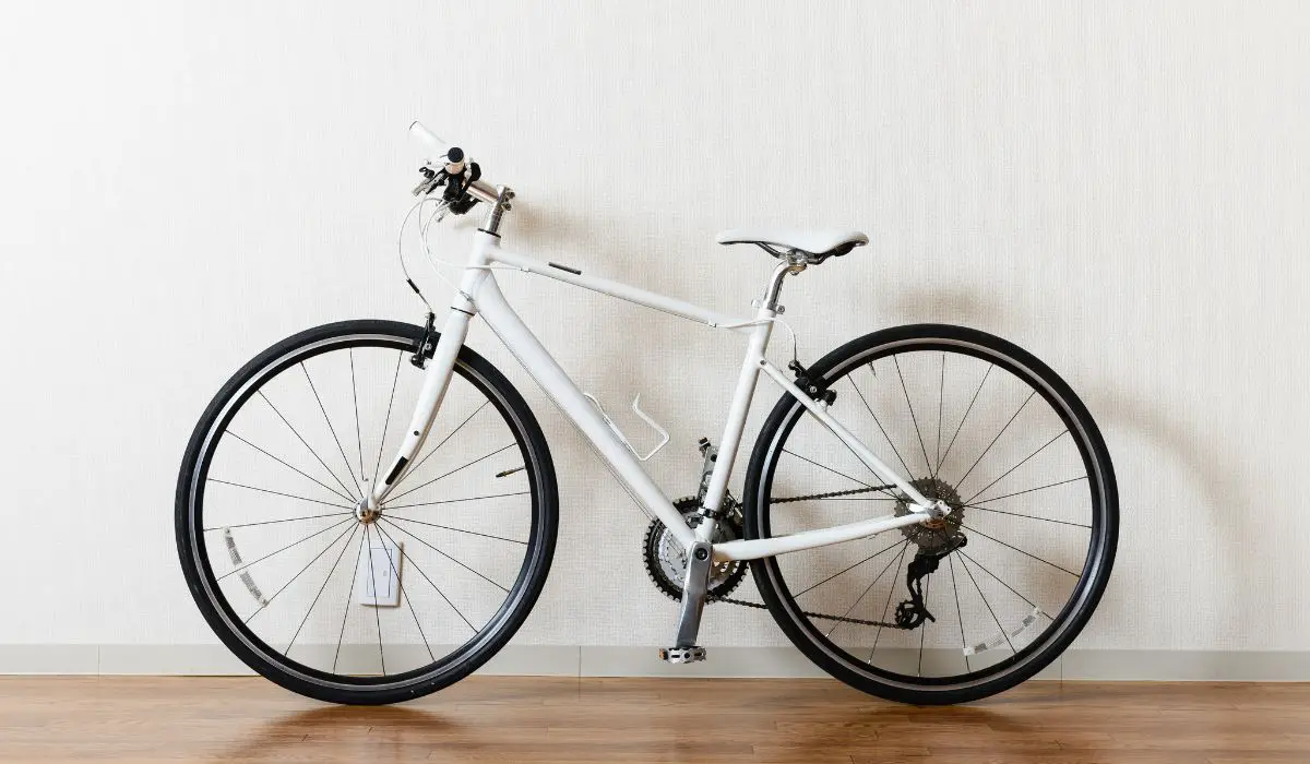 A nice looking bike that is white, sitting on a wood floor against an off white wall.