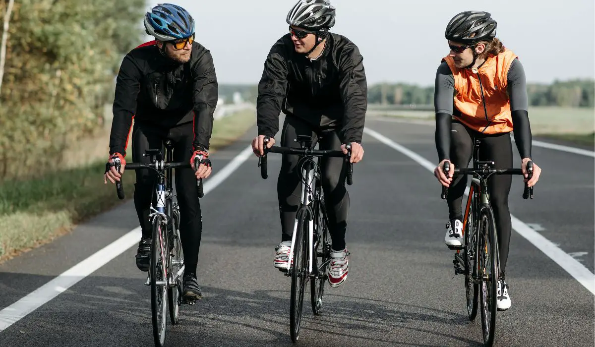 3 cyclists riding on the road in bike gear, front view. 