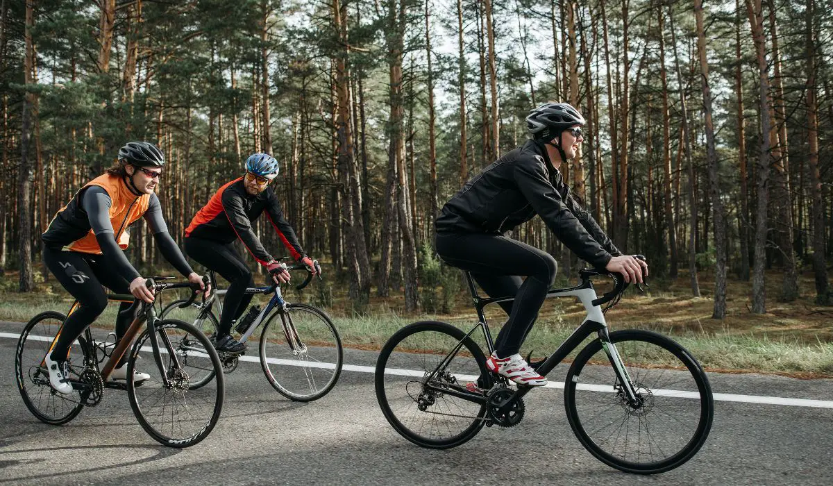  3 people riding road bikes on a forested road. 