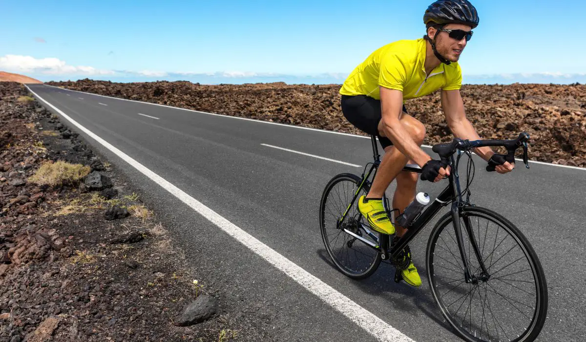 A man in a bright yellow shirt riding a road bike surrounded by rocky terrain. 