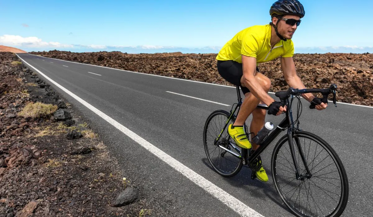 A man in a bright yellow shirt riding a road bike surrounded by rocky terrain. 