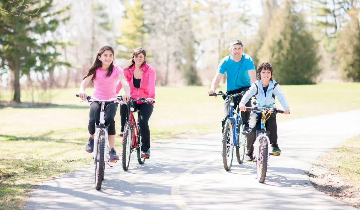 A family with 2 adults and two children riding bikes on a paved path. 