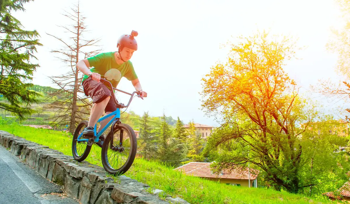 A teen on a bmx bike riding on a short stone wall. 