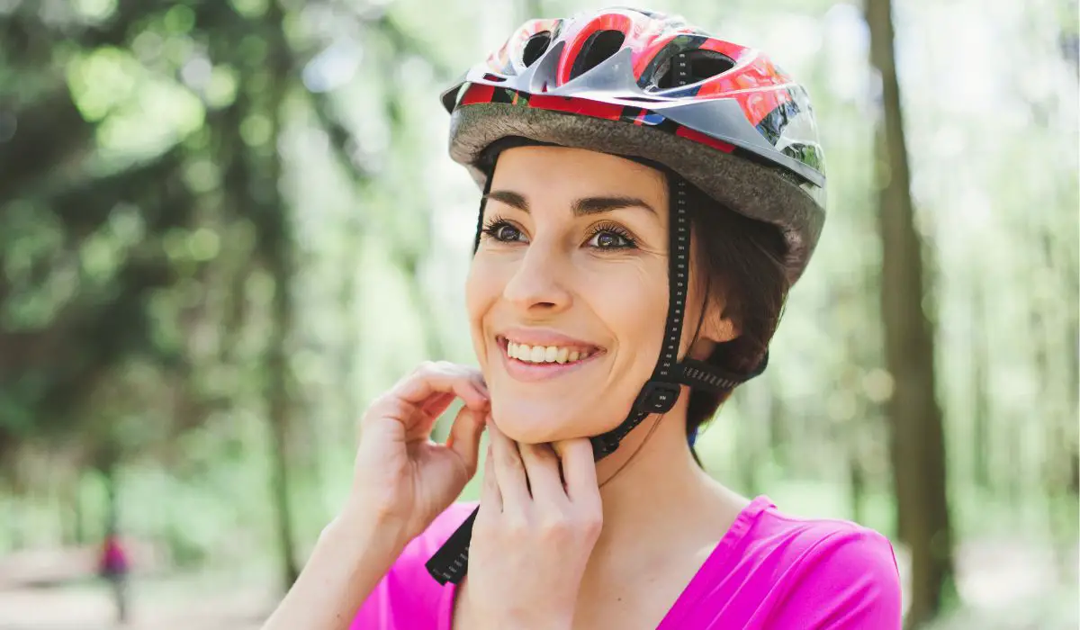 A woman putting on a bicycle helmet.