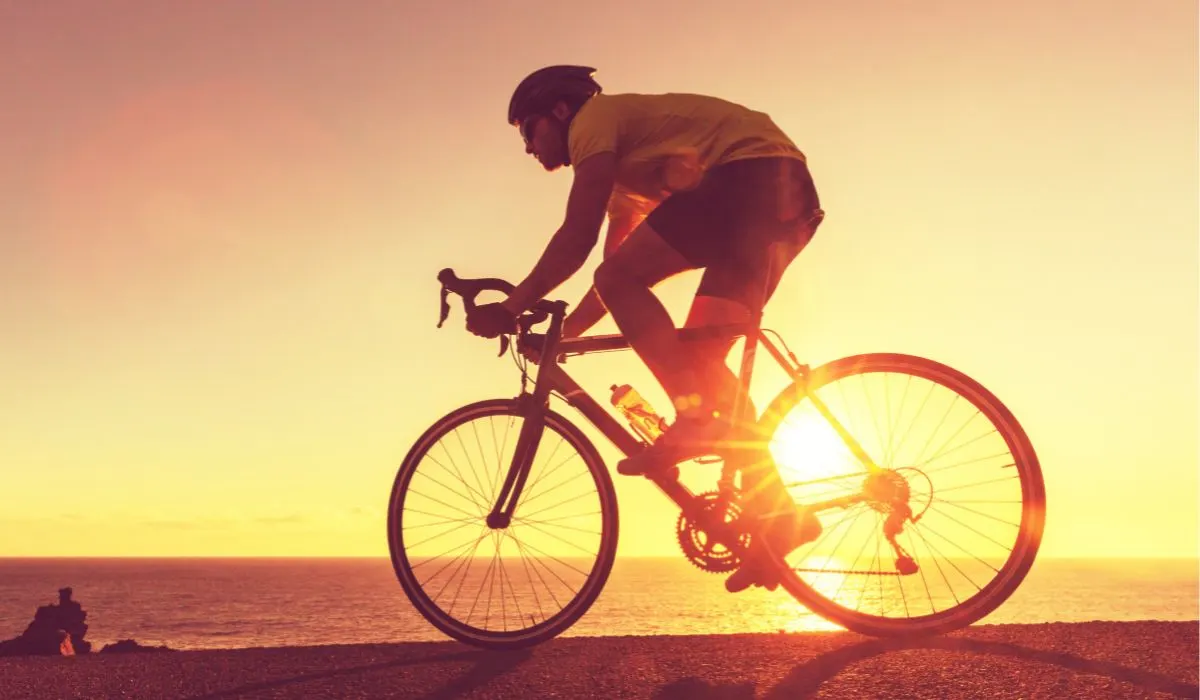 A person riding a road bike with a sunset behind them. 