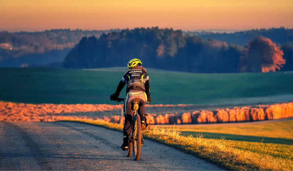 A mountain biker riding on a gravel road out in the country during a golden sunset. 