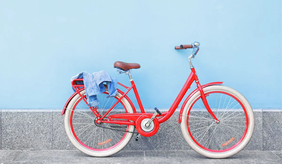 A bright red retro city bike with a brown leather seat and brown handlebars. 