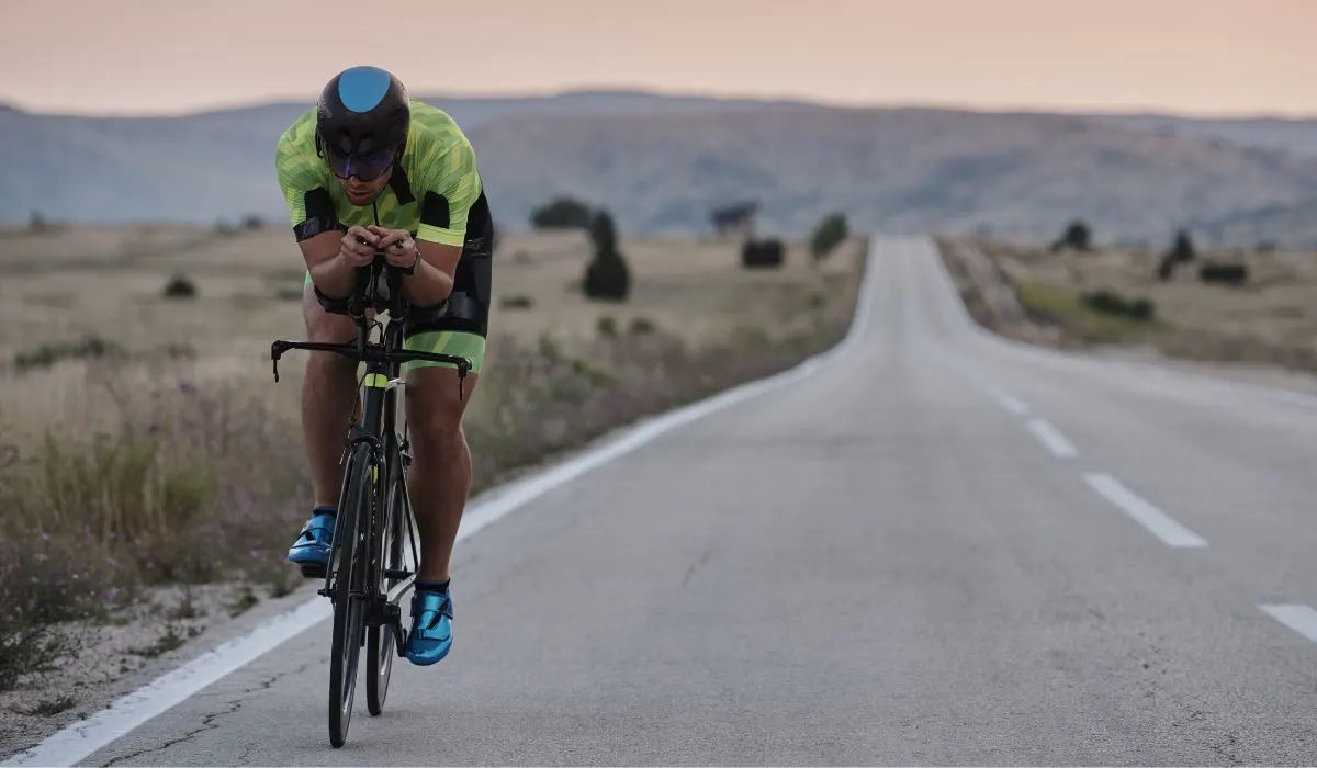 A man with a retro looking helmet on riding a road bike on a country road, front view. 