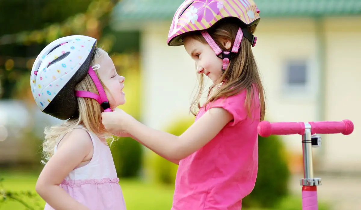 2 little girls, the older one buckling the helmet of the younger one. 