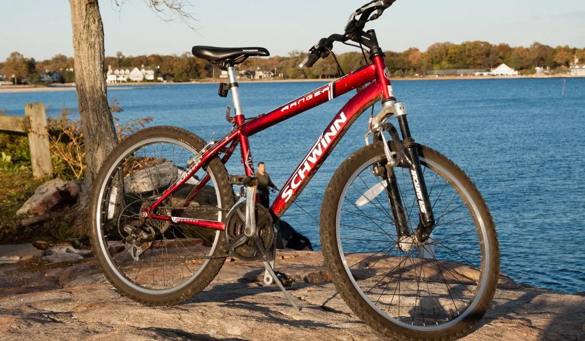 A red Schwinn mountain bike on a rocky surface next to a lake.