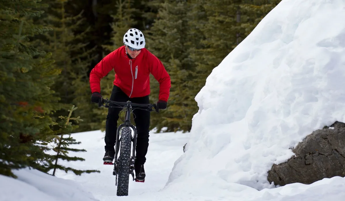 A person in a visible red coat is riding a bike in snowy weather. 