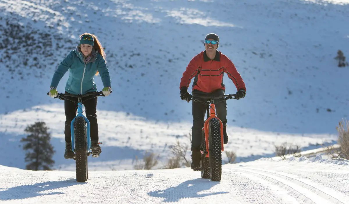 2 people riding snow bikes together on a snowy road.