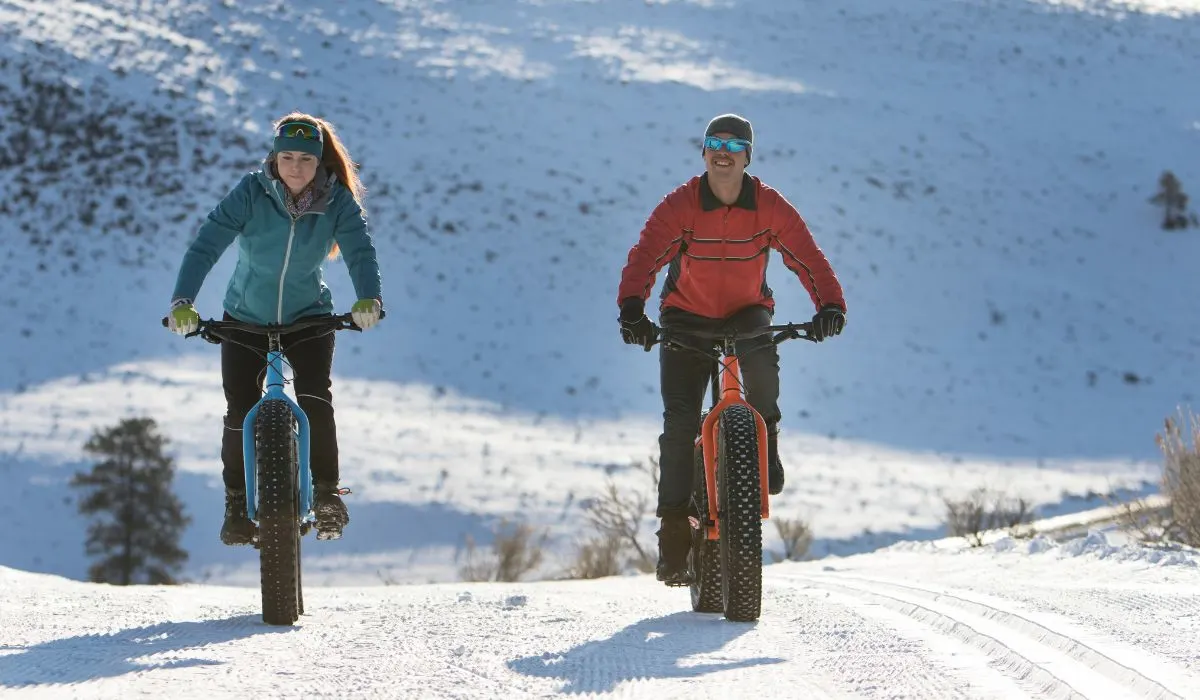 2 people riding snow bikes together on a snowy road.